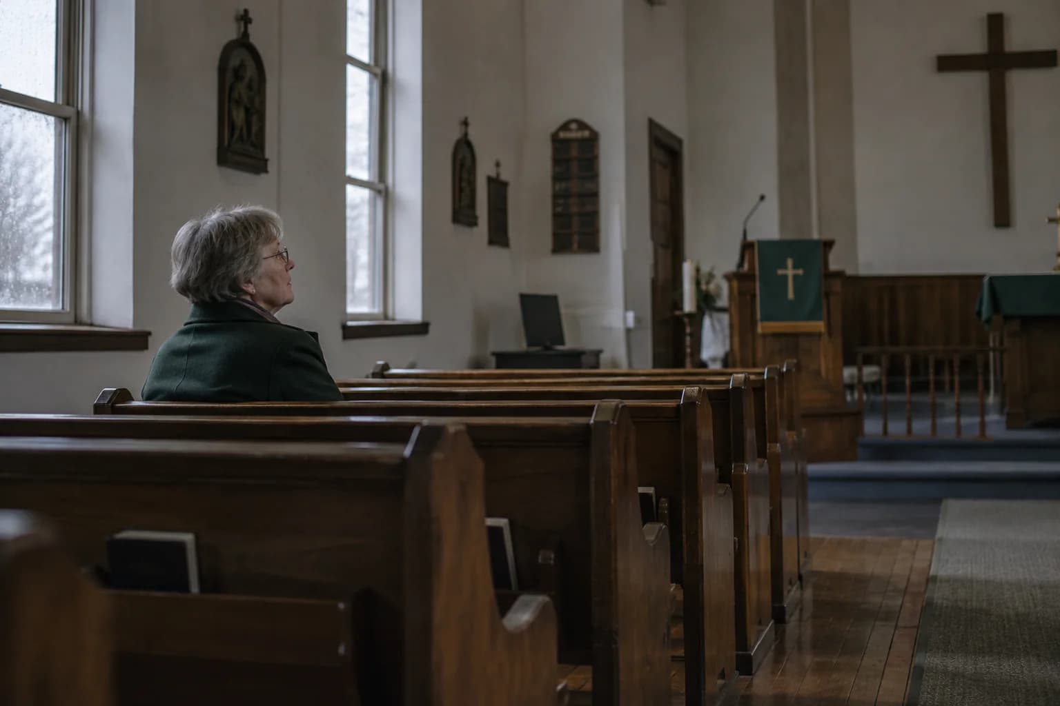 An older visitor sits quietly near the back of a church, looking toward the front.