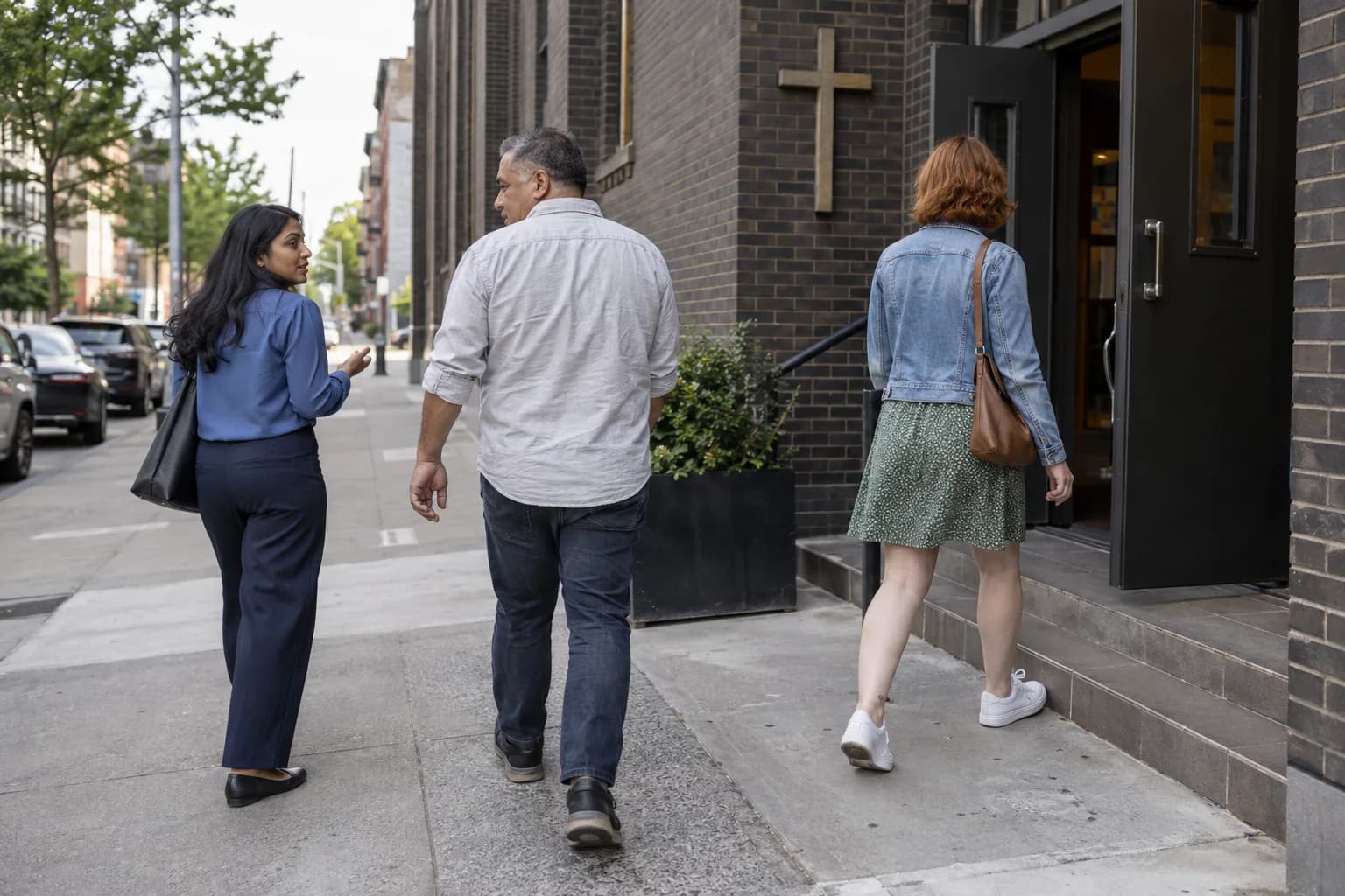 Three adults in different everyday outfits arrive at a city church.